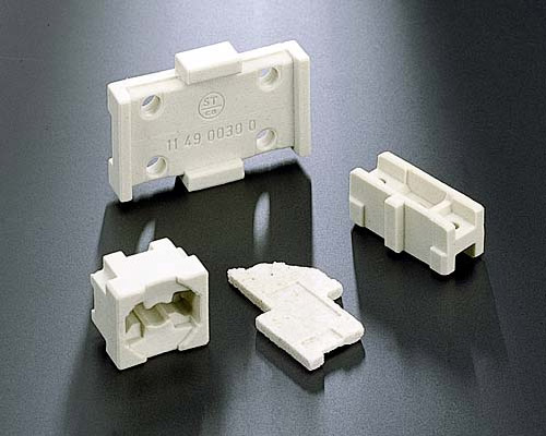 The image shows three white plastic connectors on a black surface. The connectors are arranged in a triangular formation, with the largest connector in the center and two smaller connectors on either 