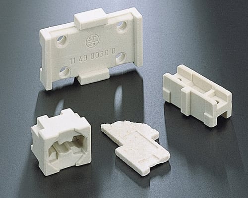 The image shows a set of three white plastic connectors on a black surface. The connectors are arranged in a triangular formation, with the largest connector in the center and two smaller connectors o
